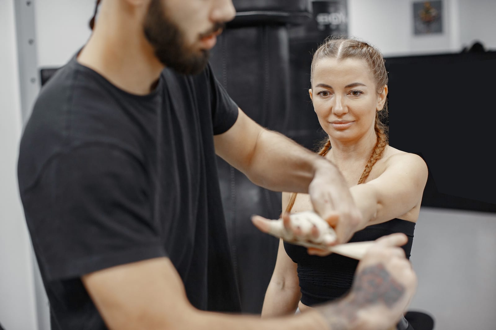 A male coach wraps the hands of a woman in black training gear before a session.