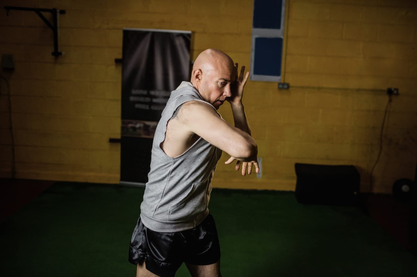 A man in a grey sleeveless top throws an elbow strike during shadow training in a gym.